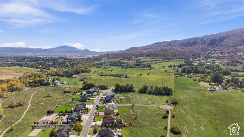 Aerial perspective of a rural residential enclave featuring expansive mountain scenery, rolling hillside terrain, and sprawling open fields