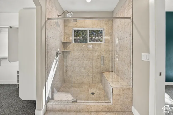 Walk-in shower featuring floor-to-ceiling tile, frameless glass enclosure, built-in tiled bench, integrated shelving, and adjustable chrome showerhead
