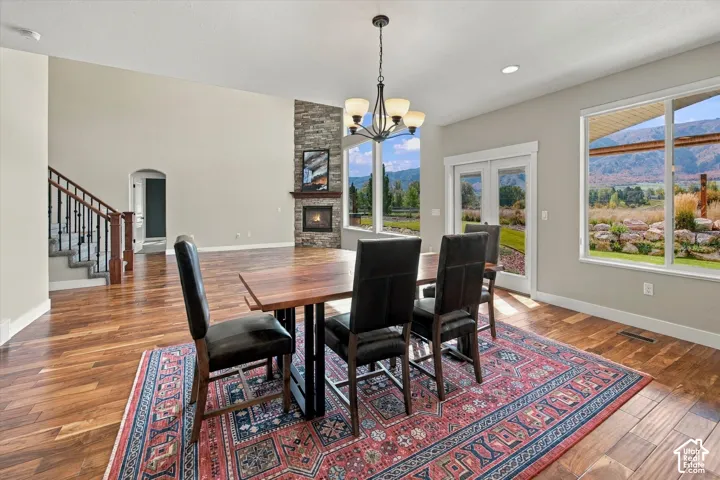 Open-concept space featuring wood-finish flooring, a floor-to-ceiling stone-surround fireplace, large windows with mountain scenery, and a wrought-iron staircase railing