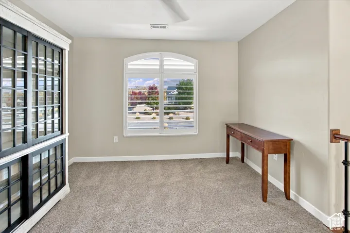Built-in display cabinetry with glass-paneled doors, arched window featuring horizontal shutters, and neutral carpeting