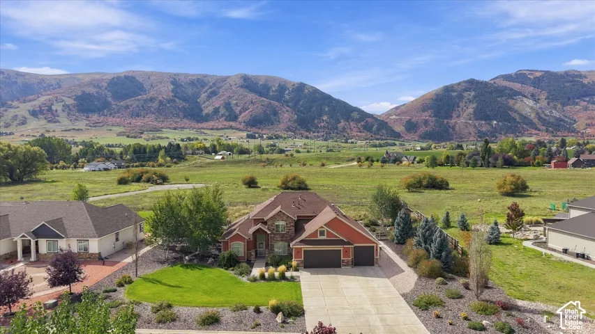 Aerial view of residential property featuring a multi-gabled roofline, stone and siding exterior, attached three-car garage, concrete driveway, and expansive mountainous backdrop