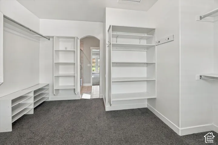 Walk-in closet featuring white built-in shelving, low-profile shoe racks, integrated clothing rods, and wall-mounted garment hooks