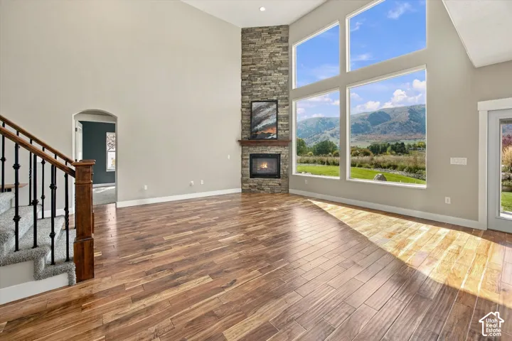 Vaulted ceilings, floor-to-ceiling stone-surround fireplace, expansive wall of windows with mountain scenery, and wood-finish flooring