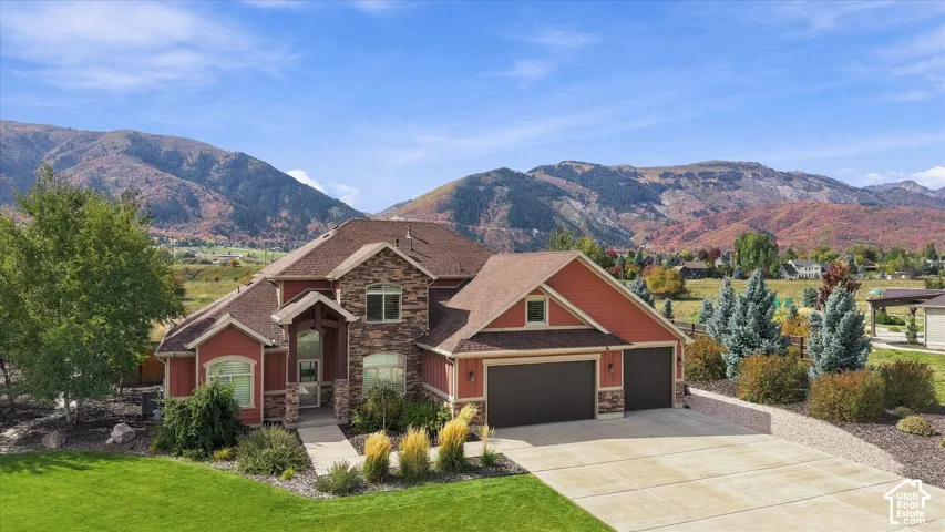 Multi-gabled exterior featuring stone masonry accents, a three-car garage, concrete driveway, and a mountain backdrop