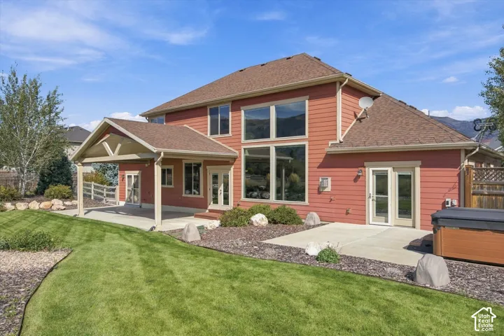 Rear elevation featuring horizontal siding, a covered patio with a gable roof, large multi-pane windows, a secondary concrete patio, and a fenced yard