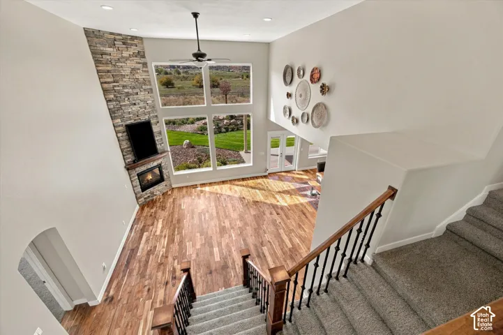 Double-height ceiling, corner stone-surround fireplace, wood-finish flooring, multi-pane floor-to-ceiling windows, and staircase with wrought iron balusters