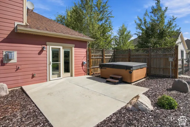 Concrete patio featuring a built-in hot tub, enclosed by wood privacy fencing with lattice detail