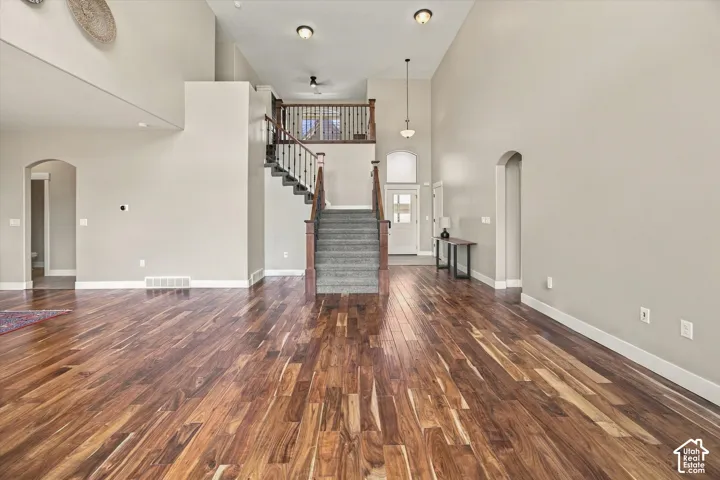 Open-concept main area featuring high ceilings, wood-finish flooring, a staircase with a wood railing, and arched doorways