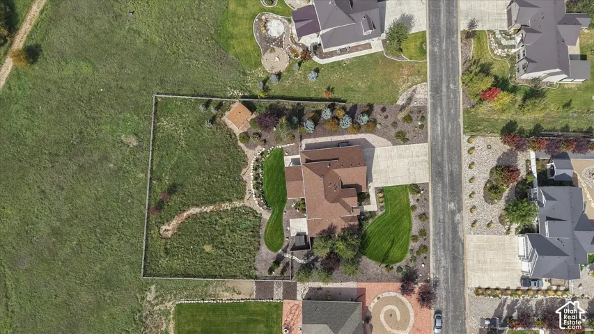Aerial perspective of a property featuring a fenced perimeter, concrete driveway, stone-paved walkway, manicured lawn areas, and established landscaping