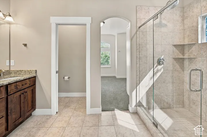 Bathroom featuring a walk-in shower with floor-to-ceiling stone-finish tile, glass enclosure, built-in shelving, wood-finish vanity with stone-finish countertop, and arched doorway entry
