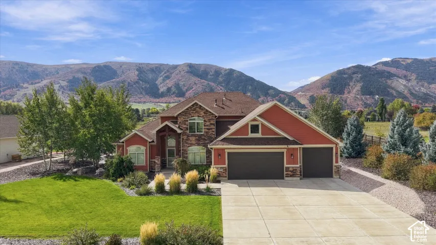 Two-story residence featuring stone and siding exterior, multi-gabled roofline, three-car garage, concrete driveway, and mountain backdrop