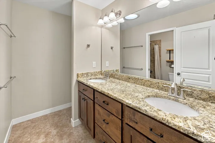 Dual-sink vanity featuring stone-finish countertops, dark wood-finish cabinetry, undermount oval basins, and polished metal fixtures