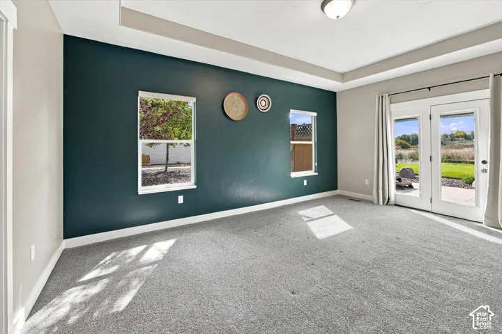 Interior room featuring a tray ceiling, dual-tone wall finishes, neutral carpeting, and a set of glass-paned double doors