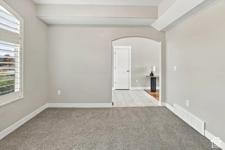 Room featuring neutral carpeting, an arched entryway, a recessed ceiling detail, and a window with plantation-style shutters