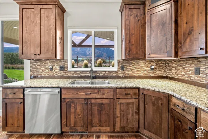Kitchen featuring stained wood cabinetry, stone-patterned countertops, mosaic tile backsplash, stainless steel dishwasher, and a dual-basin undermount sink