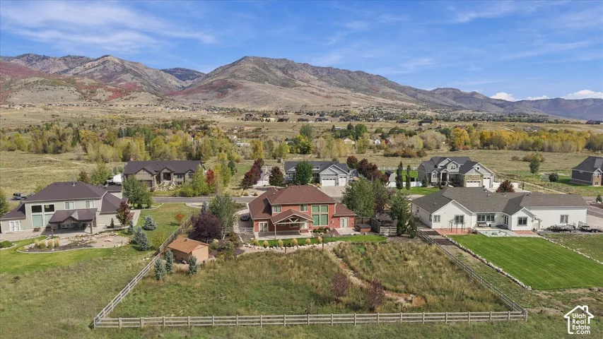 Aerial perspective featuring an expansive lot with perimeter post-and-rail fencing, a covered rear patio, and a backdrop of mountain scenery