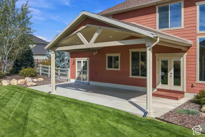Covered concrete patio featuring structural support beams, recessed lighting, and double-door entry points
