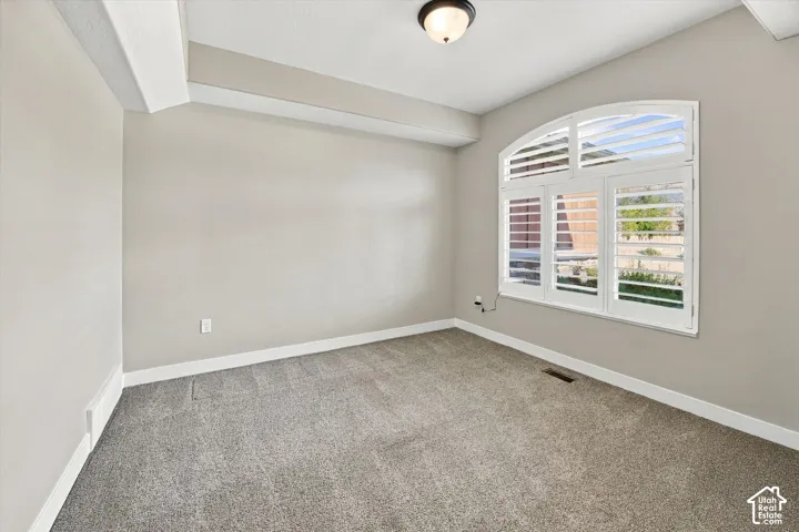 Neutral-toned room featuring plush carpeting, an arched window with plantation-style shutters, and a flush-mount light fixture