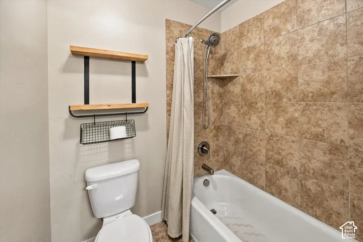 Bathroom featuring a porcelain tub, textured tile shower surround, integrated corner soap shelf, handheld shower head, and wall-mounted wooden shelving unit