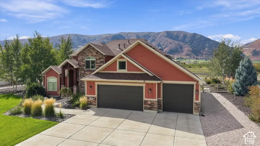 Multi-gabled exterior featuring stone veneer, horizontal siding, a three-car garage, and concrete driveway set against a mountain backdrop