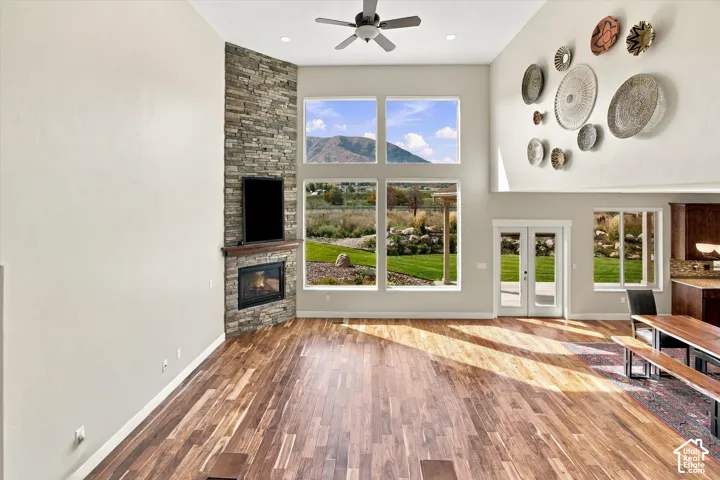 Vaulted ceilings with a ceiling fan, full-height stone fireplace, wood-finish flooring, large-format windows, and double glass-pane doors