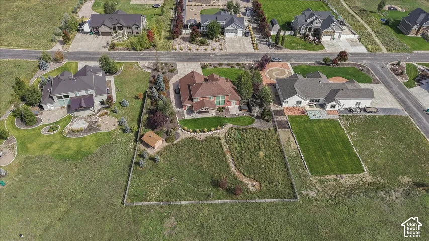 Aerial perspective featuring a multi-level residence with a multi-gabled roof, stone and brick exterior, paved driveway, expansive lawn, and detached storage structure on a fenced lot
