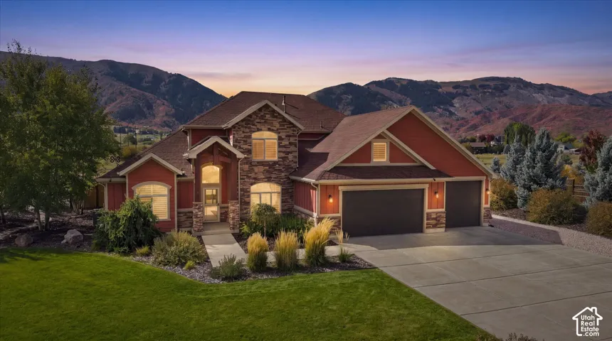 Multi-level exterior featuring stone veneer siding, arched window detailing, an attached three-car garage, and a concrete driveway, set against a mountain backdrop