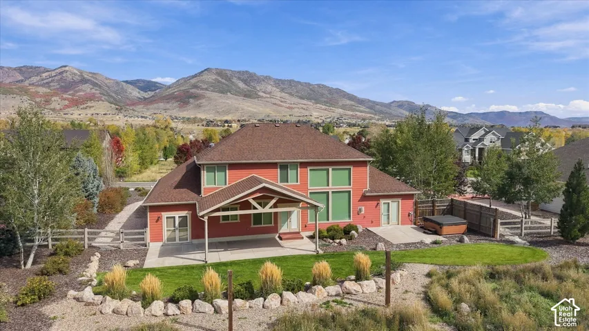 Multi-level residence featuring a covered rear patio, integrated hot tub, tiered landscaping with stone borders, and mountain backdrop