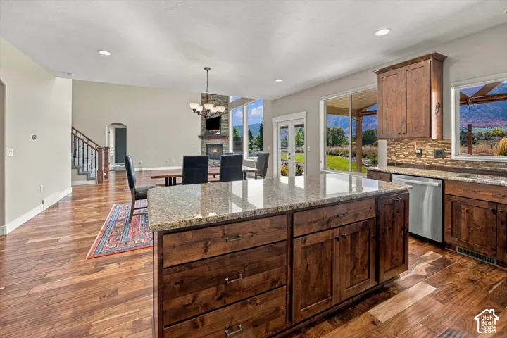 Kitchen featuring an expansive stone-topped island, rich-toned custom cabinetry, wood-finish flooring, stainless steel appliances, and a tiled backsplash