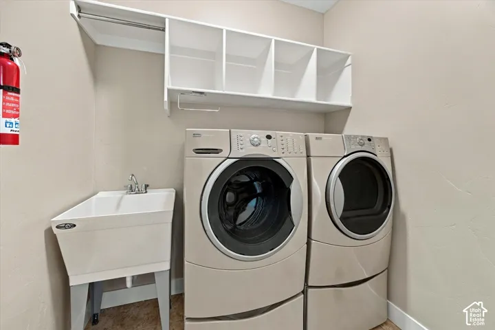 Laundry space featuring a built-in white storage shelf with integrated hanging rod, a white utility sink with dual-handle faucet, and washer and dryer hookups