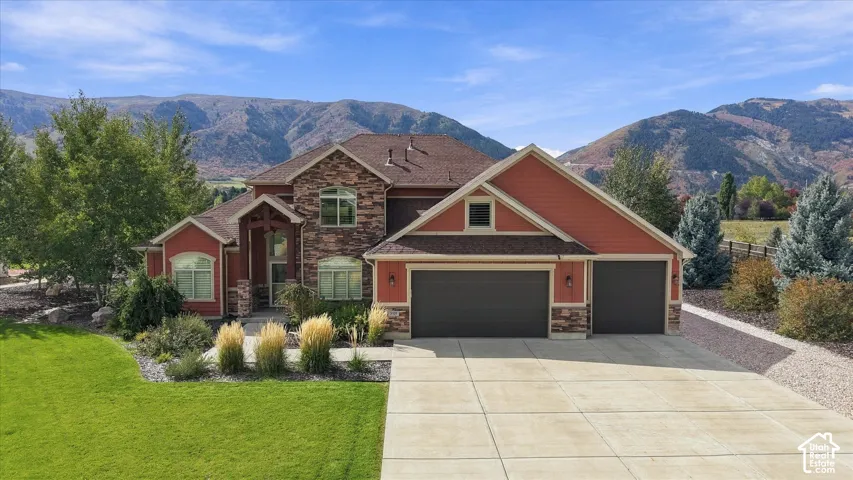 Multi-level residence featuring stone and horizontal siding exterior, attached three-car garage, concrete driveway, and expansive mountain backdrop