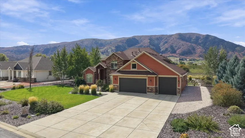 Multi-level residence featuring stone and siding exterior, expansive concrete driveway, three-car garage, and mountain backdrop