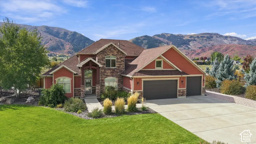 Custom-built exterior featuring stone veneer accents, shingle roof, three-car garage, and prominent mountain backdrop