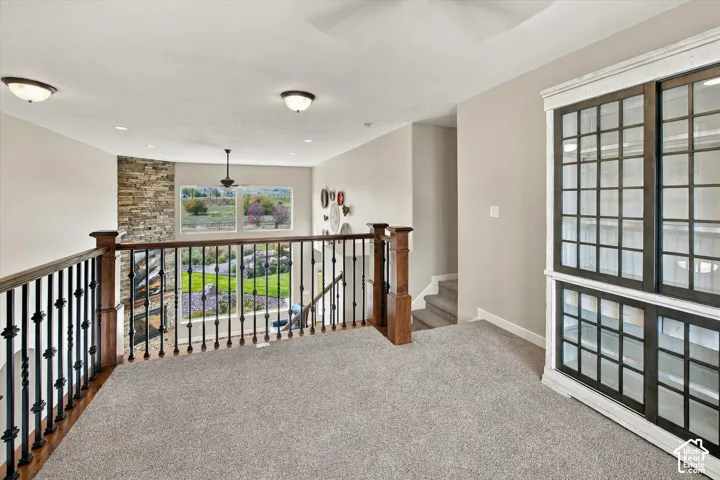 Open loft area featuring a built-in display cabinet with multi-pane glass doors, stacked-stone accent wall, wood-capped iron railing, and recessed lighting