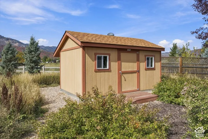 Detached storage structure featuring vertical siding, asphalt shingle roofing, dual windows, and a wood-plank entrance platform