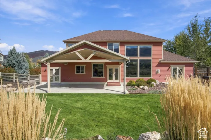 Covered rear patio featuring timber-frame accents, concrete flooring, exterior siding, large multi-pane windows, and a landscaped lawn