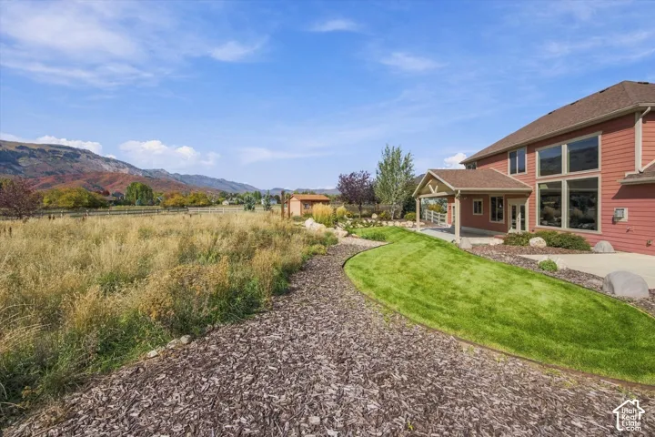 Rear exterior featuring horizontal lap siding, a covered patio, manicured lawn, wood-chip landscaping, and a mountainous backdrop