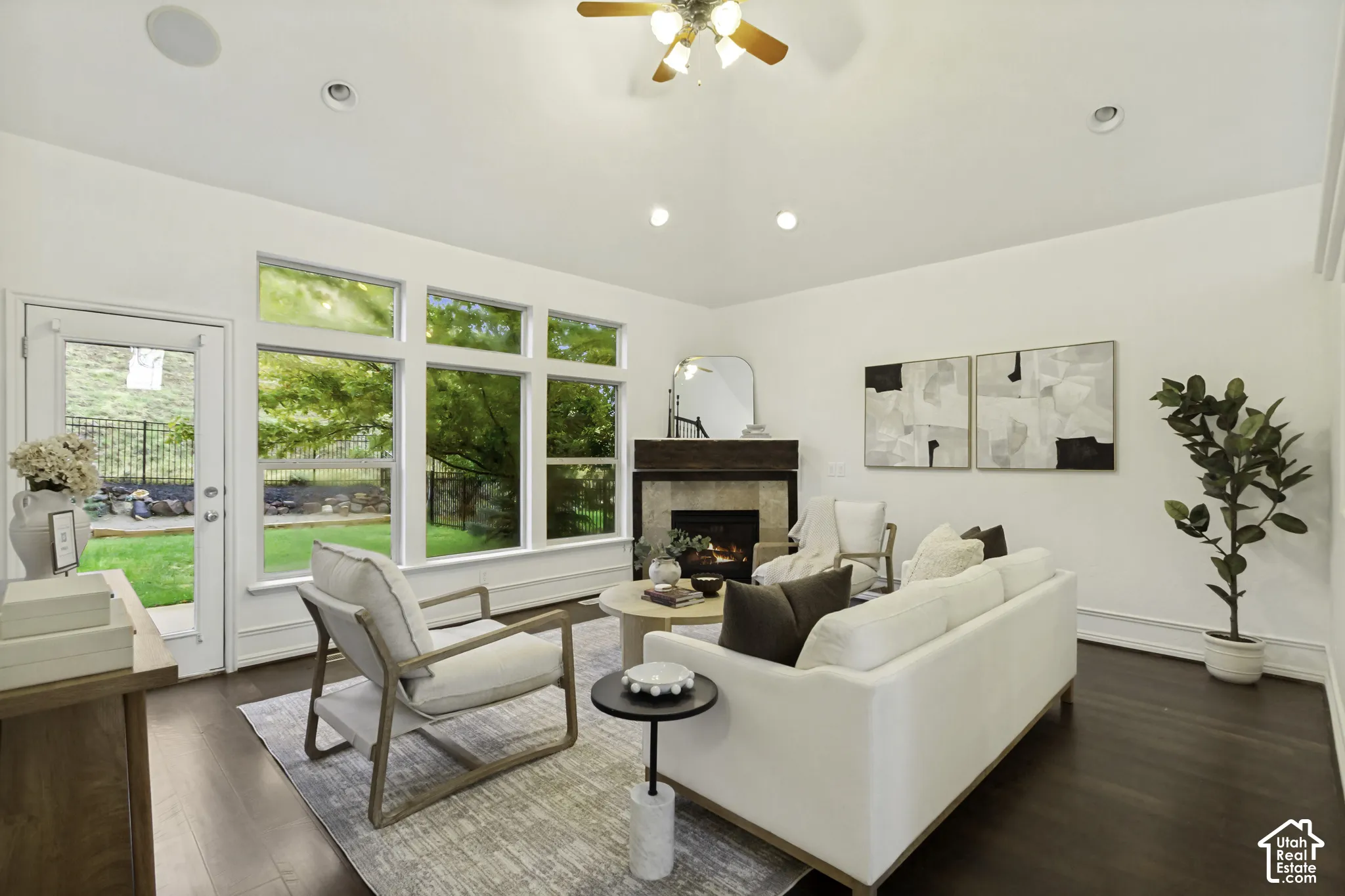 Vaulted ceilings featuring recessed lighting and a ceiling fan, wood-finish flooring, large multi-pane windows, and a fireplace with a stone surround and timber mantel