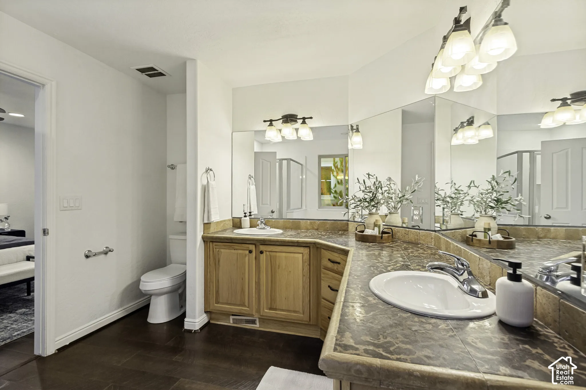 L-shaped vanity with tile countertop, dual recessed oval sinks, natural wood-finish cabinetry, and oversized wall-to-wall mirrors