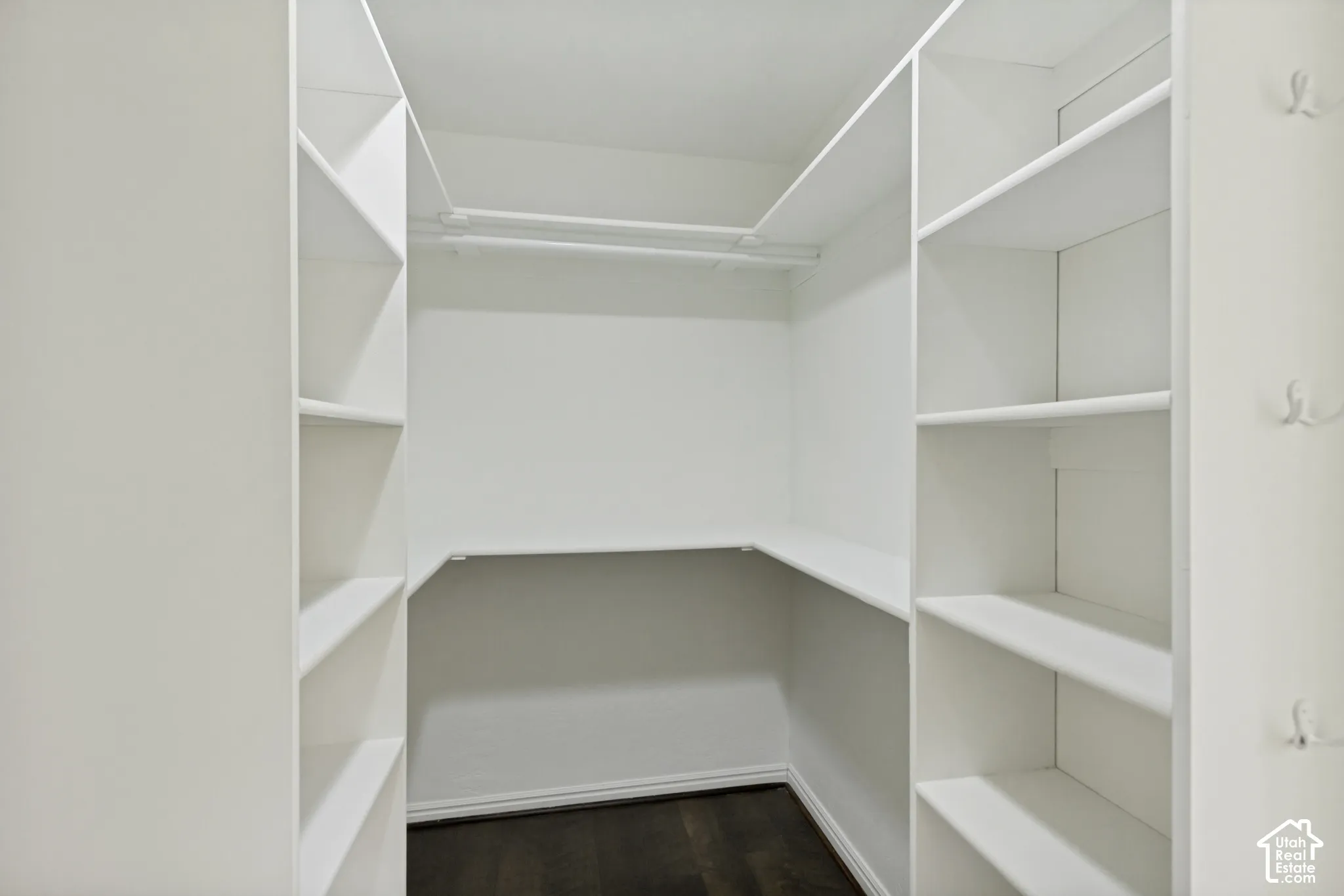 Walk-in closet featuring white built-in shelving, integrated hanging rods, wall-mounted hooks, and wood-finish flooring