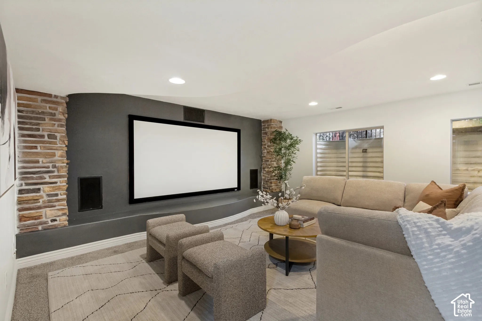 Media room featuring a curved accent wall, built-in display screen, recessed stone columns, integrated speakers, and carpeted flooring