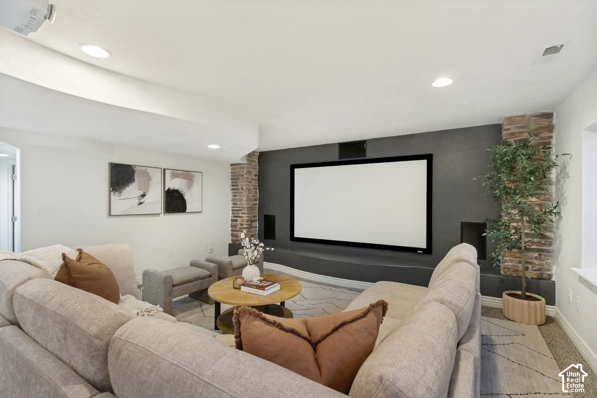 Media room featuring a recessed projection screen, stone-accented columns, a custom built-in low-profile media shelf, integrated wall speakers, and recessed ceiling lighting