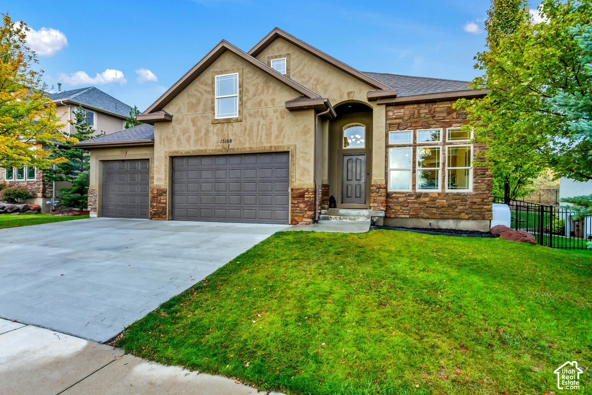 Exterior facade featuring a combination of stucco and natural stone veneer, a multi-gabled roofline, an arched entryway, and a three-car garage