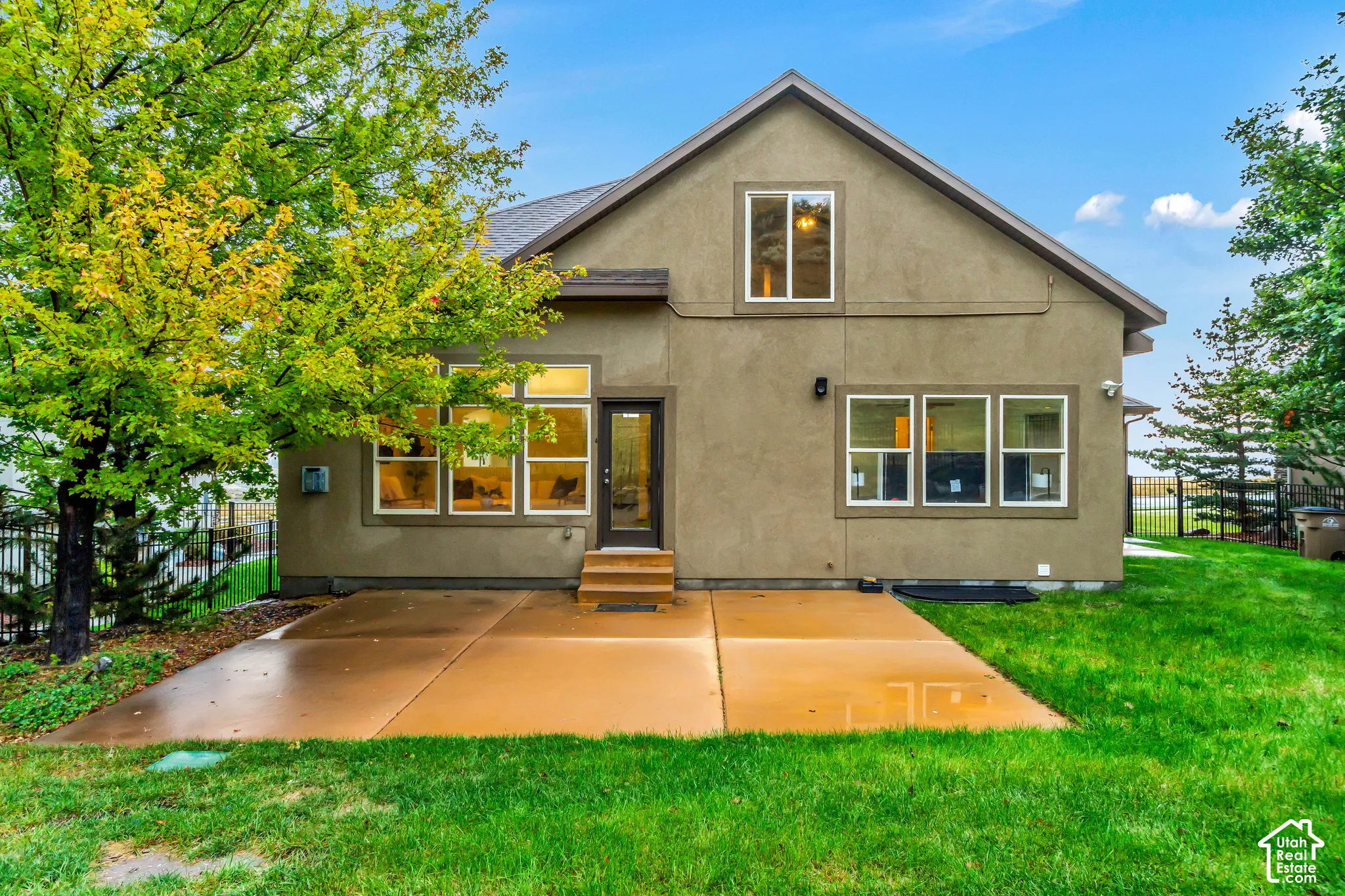 Stucco exterior featuring a concrete rear patio, multiple large window groupings, and a manicured lawn