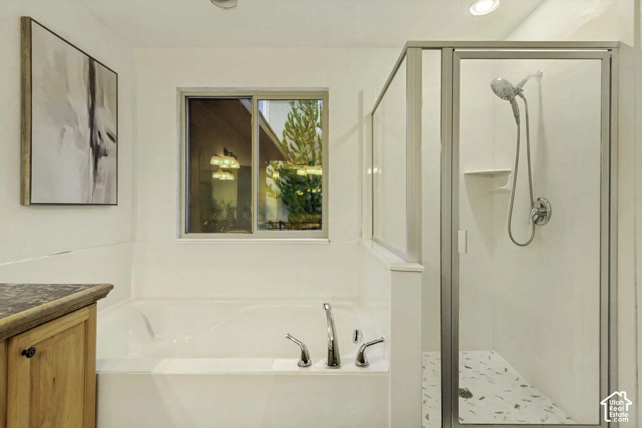 Soaking tub with chrome faucet fixtures, separate shower enclosure with a handheld showerhead, and wood-finish cabinetry