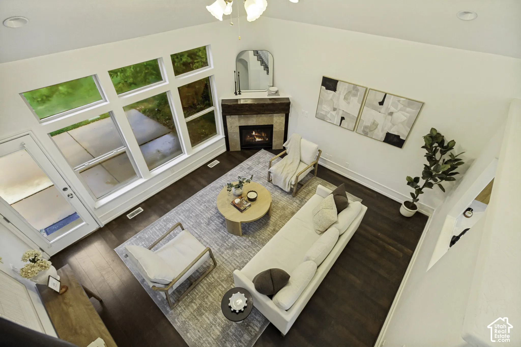 Vaulted ceilings, dark wood-finish flooring, corner fireplace with a stone-tile surround, and expansive multi-pane windows