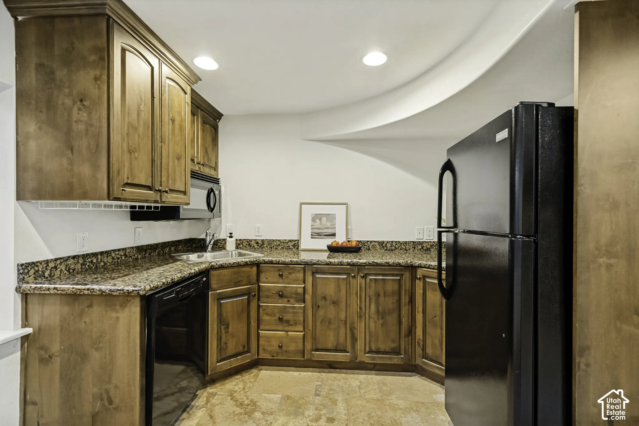 Stained wood cabinetry, stone countertops, recessed lighting, and black appliances