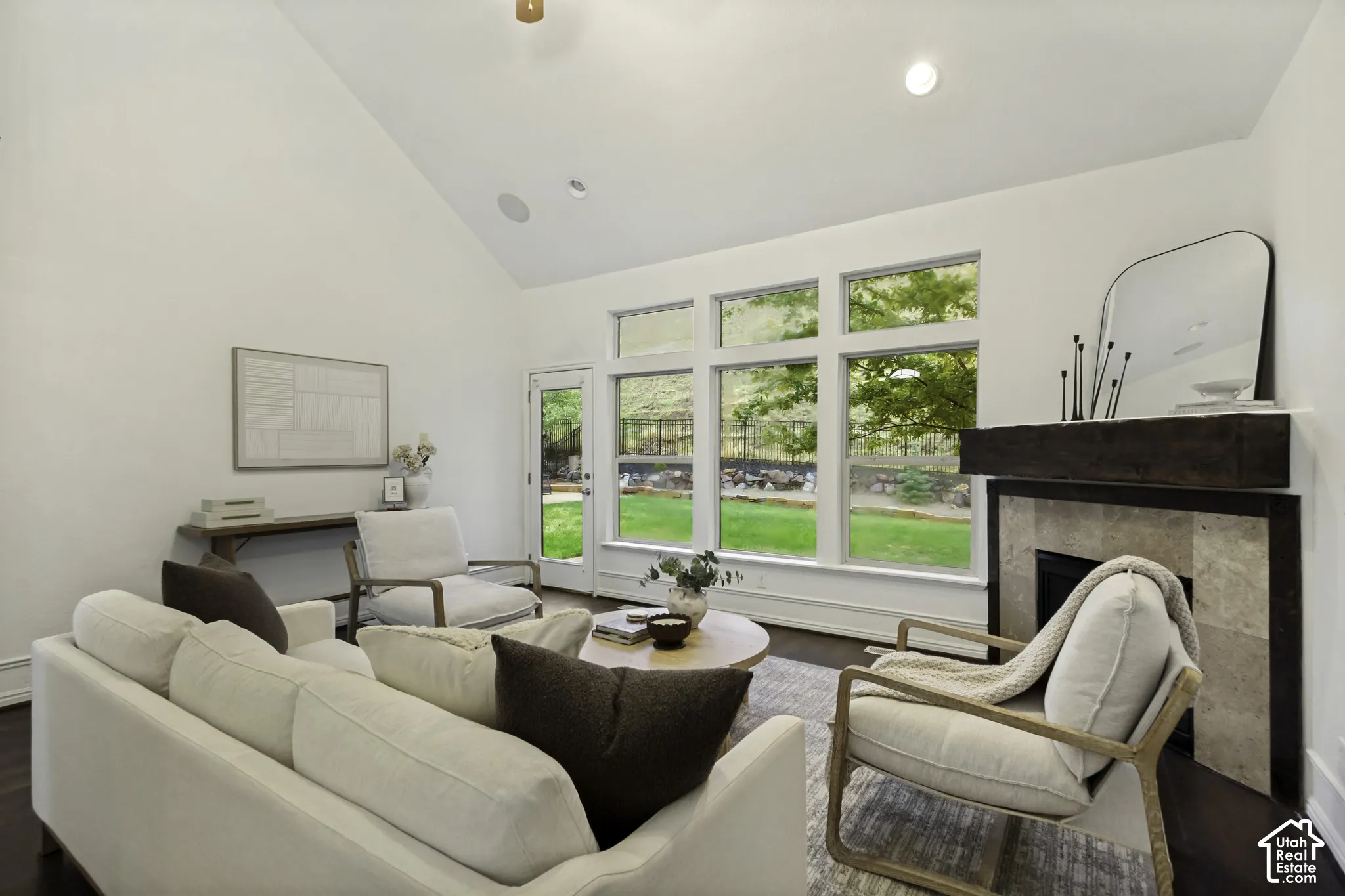 Vaulted ceilings, expansive windows, fireplace with stone surround and timber mantel, recessed lighting, and wood-finish flooring