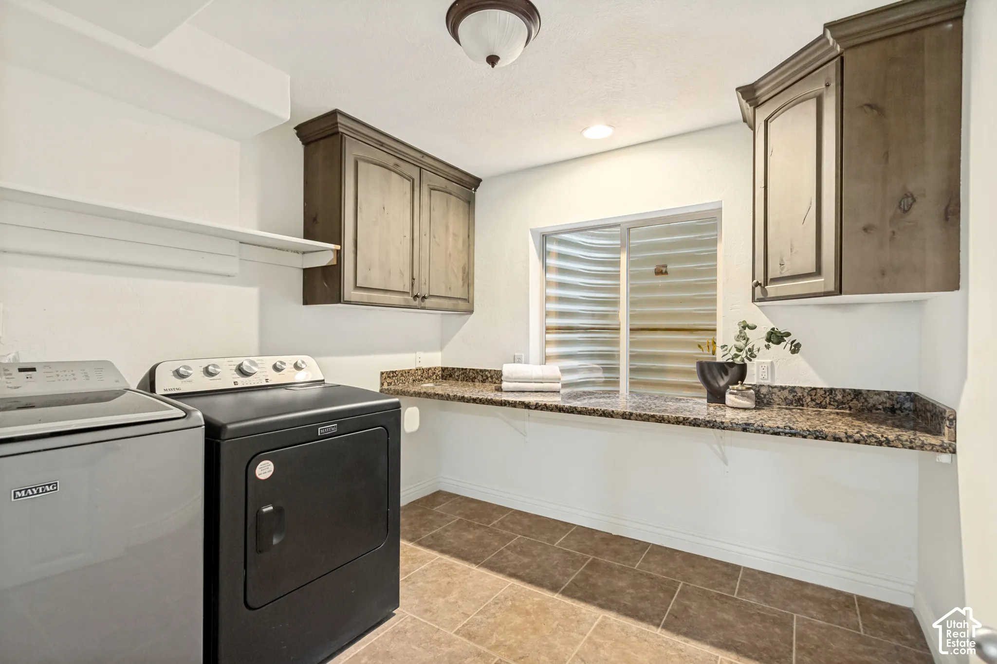 Laundry area featuring stained wood cabinetry, stone-surface countertop, tile flooring, and a recessed window