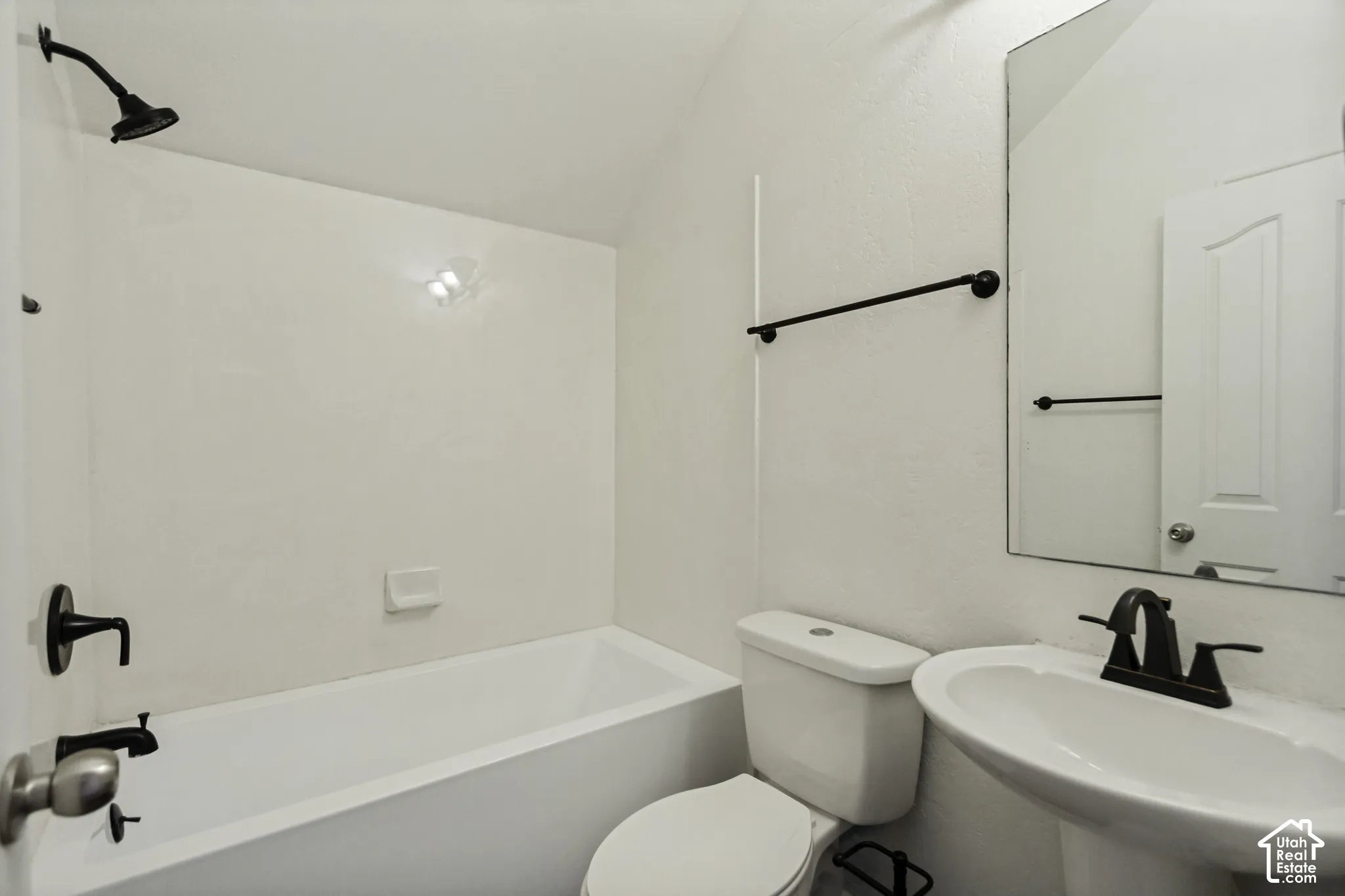 Bathroom featuring a white pedestal sink, porcelain tub, shower head with matte black hardware, and an oversized wall-mounted mirror